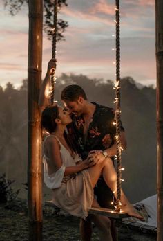 a man and woman sitting on a swing with string lights hanging from the strings around them