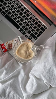 an open laptop computer sitting on top of a white bed next to a cup of coffee