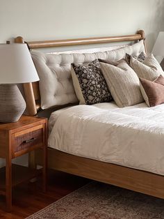 a bed with many pillows on top of it and a night stand next to it