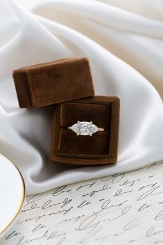 an engagement ring in a velvet box on top of a white satin cloth covered table