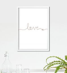 a white frame with the word love in cursive writing on it next to some plants