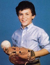 a young man holding a baseball and glove in front of a blue background with the ball in his hand