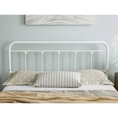 a white metal headboard and foot board in a room with light blue walls, striped throw pillows and decorative artwork on the wall