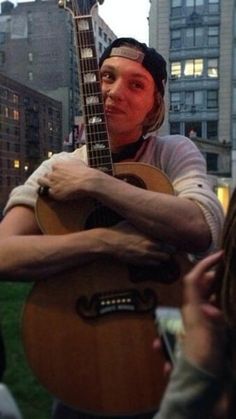 a man is playing an acoustic guitar on the street while people are looking at him