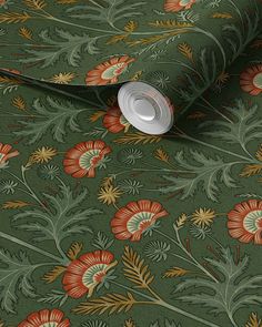 a green floral wallpaper with red, orange and yellow flowers on the ground next to a roll of toilet paper