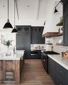 a large kitchen with black cabinets and white counter tops, wooden flooring and hanging lights