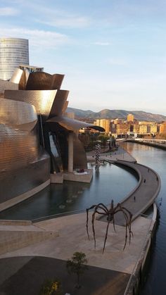 a large spider sculpture sitting on top of a river next to a cityscape