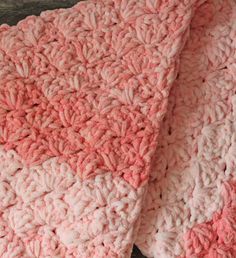 pink and white crocheted blanket sitting on top of a wooden table