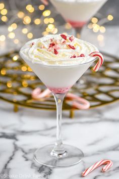 two glasses filled with whipped cream and candy canes on a marble counter top next to christmas lights