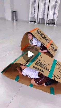 two children are playing with cardboard boxes on the floor