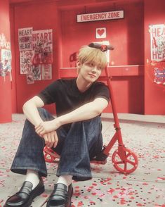 a young boy sitting on the ground next to a scooter in a red room