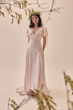 a woman in a wedding dress standing under a tree branch with her hands on her hips