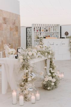 a table with white flowers and candles on top of it next to a bar filled with liquor bottles