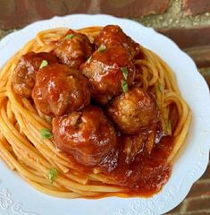 spaghetti with meatballs and sauce on it sitting on a white plate next to a brick wall