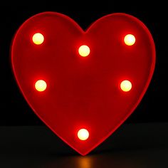 a red heart shaped light up sign sitting on top of a black table with white dots