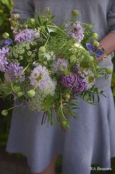 a woman holding a large bouquet of flowers in her hands and wearing a gray dress