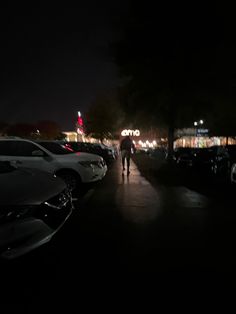 a person walking down a street at night with cars parked on the side of the road