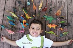 a young boy standing in front of a bunch of toy dinosaurs on a wooden floor