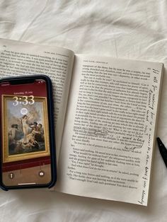 an open book sitting on top of a bed next to a cell phone