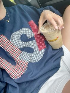 a person sitting in the back seat of a car holding a drink and wearing a tshirt