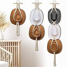 three hats hanging from hooks on the wall next to a wicker chair and potted plant