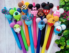 several different colored mickey mouse pens are lined up on a white surface with flowers in the background