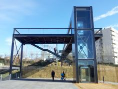 two people are walking under an overpass in front of a building with a walkway