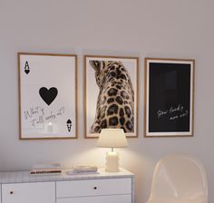 two framed pictures hang on the wall next to a white dresser with a chair and lamp