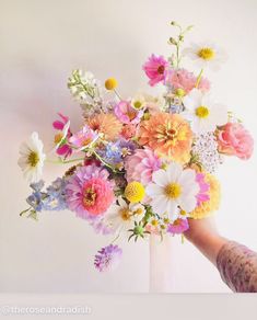 a person holding a bouquet of flowers in front of a white wall with pink, yellow and blue flowers