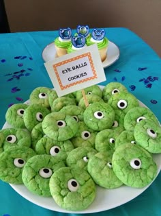 some green cookies with googly eyes are on a plate and there is a sign that says eye balls cookies