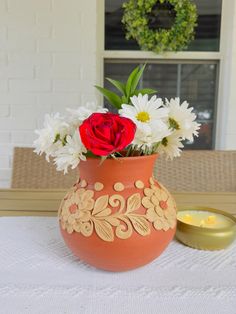 a vase filled with white and red flowers on top of a table next to a candle