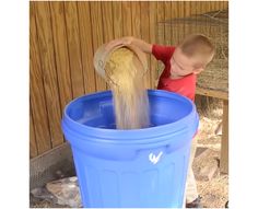 a young boy is pouring something into a blue trash can with hay in the background