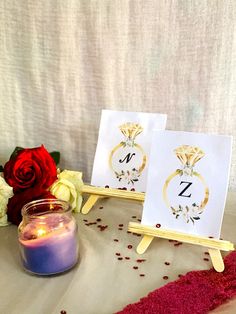 there are two cards on the table next to a candle and some red rose petals