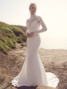 a woman in a wedding dress standing on the rocks by the ocean with her hands on her hips