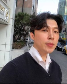 a man standing in front of a building with cars parked on the street behind him