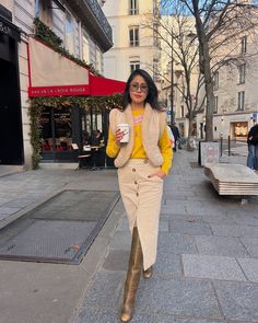 a woman is walking down the street with a cup in her hand and wearing boots