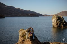 two people standing on the edge of a cliff near water