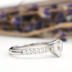 a white gold ring with diamonds on it and a purple flower in the back ground