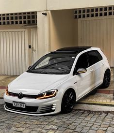 a white car parked in front of a building on a cobblestone street next to two garage doors