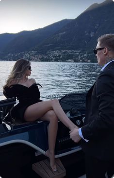 a man and woman sitting on the back of a boat in front of a body of water