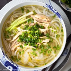 a bowl of chicken noodle soup with green onions and celery on the side