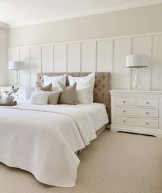 a bedroom with white bedding and pillows on the headboard, dressers and lamps