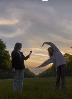 two people standing in the grass with their arms spread out and one person reaching for something