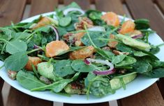 a white plate topped with spinach salad and oranges on top of a wooden table