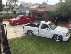 a white truck parked in front of a house next to two red trucks on the grass