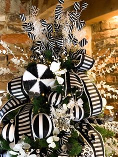 a christmas tree decorated with black and white ribbons, ornaments and greenery in front of a brick wall