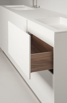 a white bathroom with two sinks and a cabinet in the middle that has an open drawer underneath it