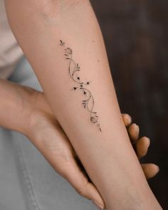 a woman's arm with a tattoo on it that has flowers and leaves in the middle