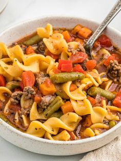 a white bowl filled with pasta and vegetables on top of a table next to a spoon