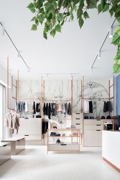 the inside of a clothing store with lots of clothes on shelves and hanging plants in front of them